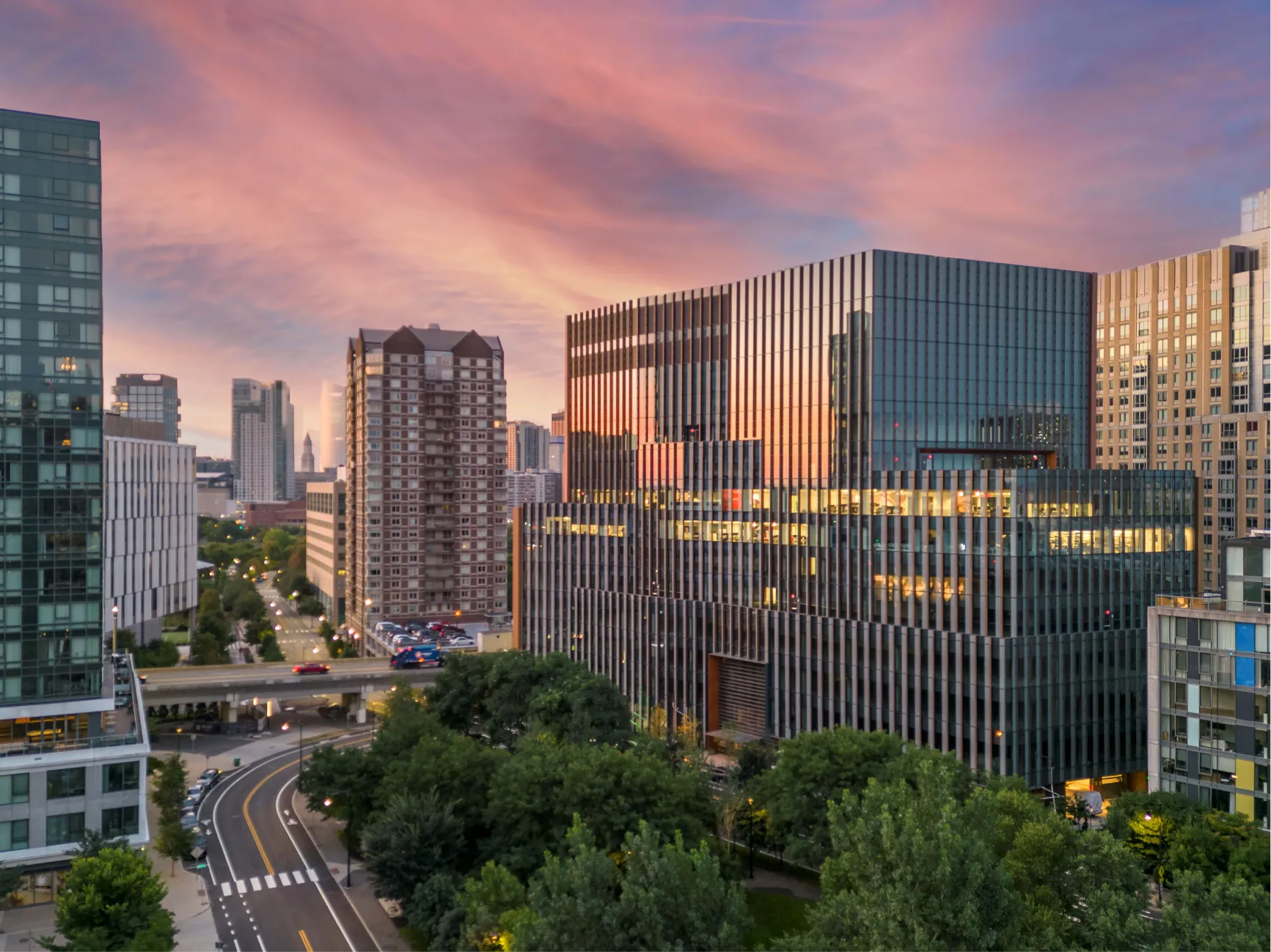 Contemporary laboratory building reflecting colorful sunset sky with urban skyline and tree lined streets below