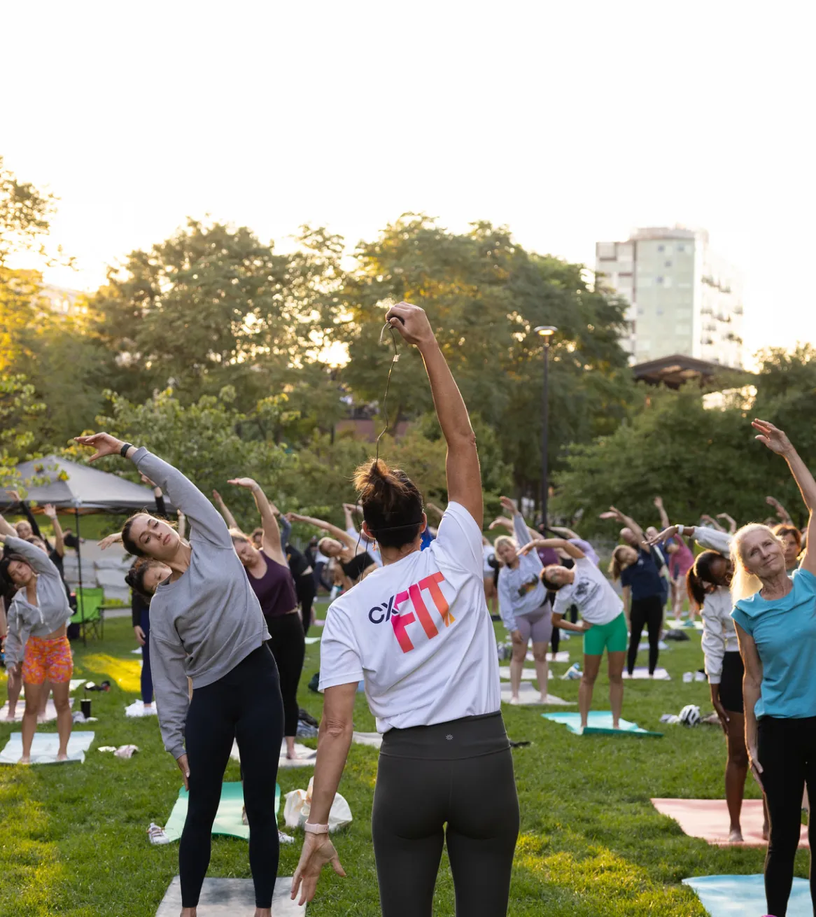 Community yoga workout in Cambridge green space with instructor leading group stretching exercises outdoors