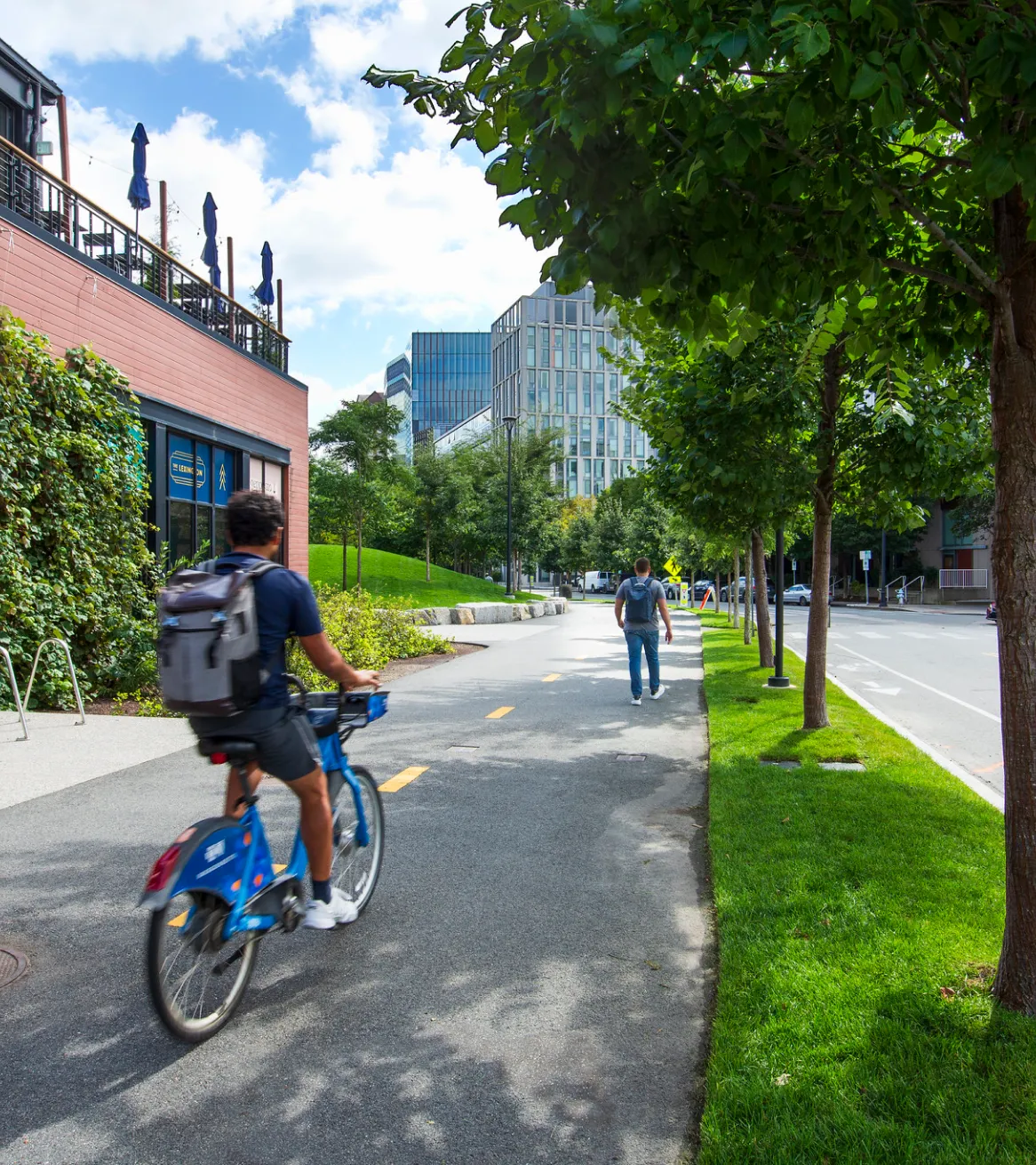 Cambridge Crossing bike path with cyclist and pedestrian along tree lined urban greenway near modern offices