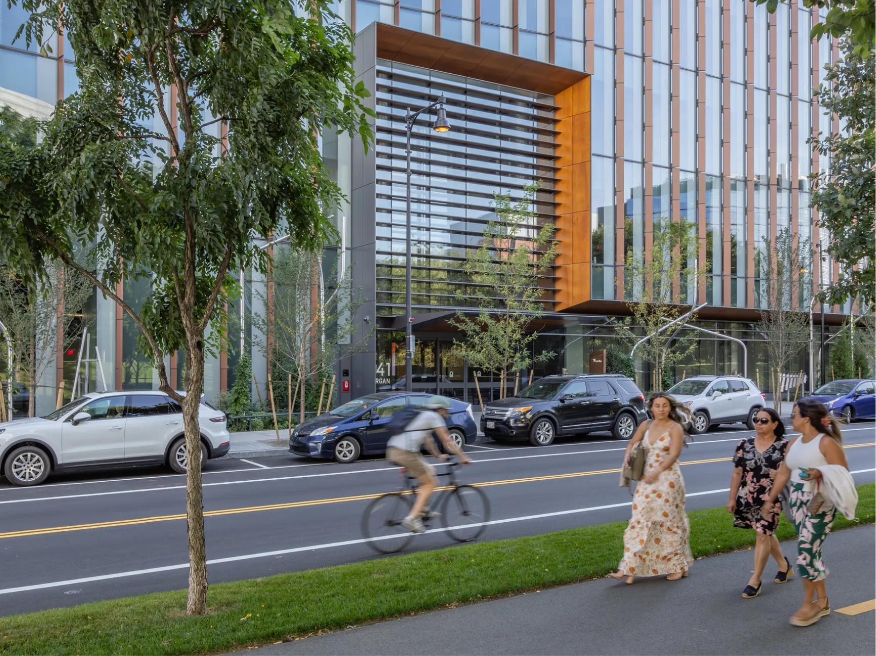 Street level view of modern glass office building with pedestrians cyclists and parked cars in urban setting